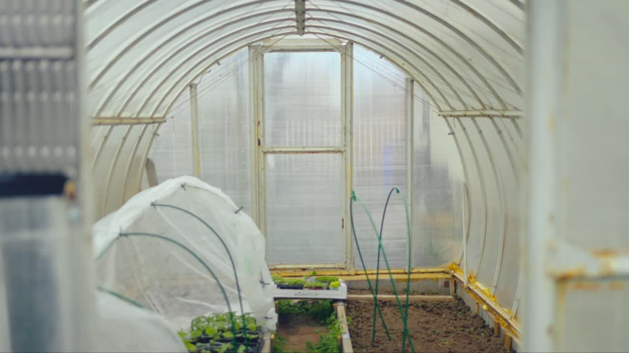 Interior of small greenhouse with mini tunnel greenhouse and planting beds inside plastic structure. Captured in Latvia, Latgale.