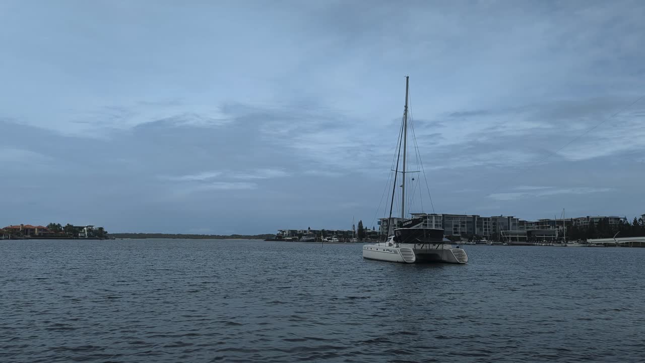 A Catamaran is anchored in the calm waters with a sea bird flying overhead.