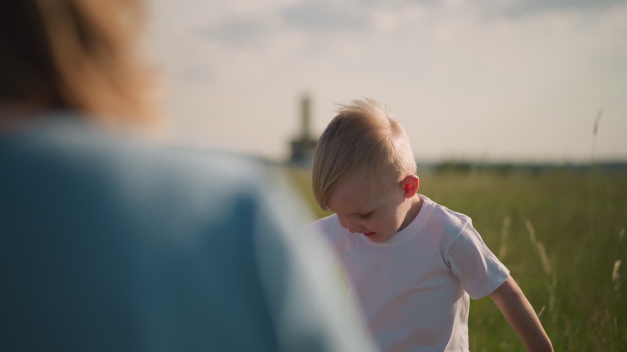 A young child in a white shirt is captured mid-jump on a sunny day, enjoying the freedom and joy of playing in a grassy field. The background is softly blurred
