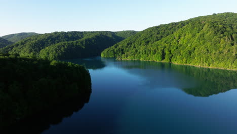 serene lake surrounded by forested hills on sunny morning in plitvice lakes national park, croatia