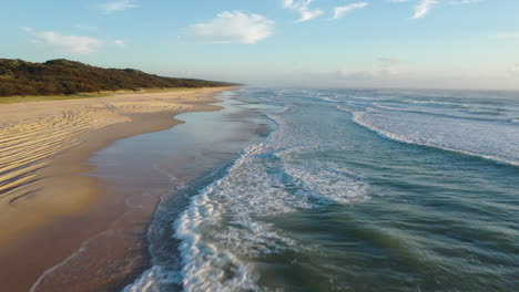 Un-Dron-Disparó-Bajo-Sobre-Olas-Tranquilas-Que-Barren-La-Playa-De-La-Isla-Fraser,-Una-Mañana-Serena-En-Australia