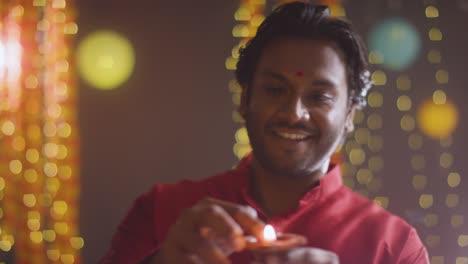 man celebrating festival of diwali holding lit diya oil lamp towards camera