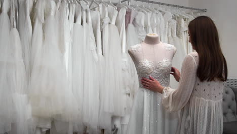 hermosa niña buscando vestido de novia en la cabina en comparación con otros vestidos. preparando para la boda. comprando un vestido de novia. la costurera inspecciona el vestido de novia hecho a medida terminado.