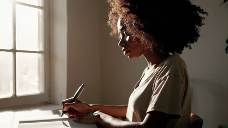 person writing in a notebook near a window