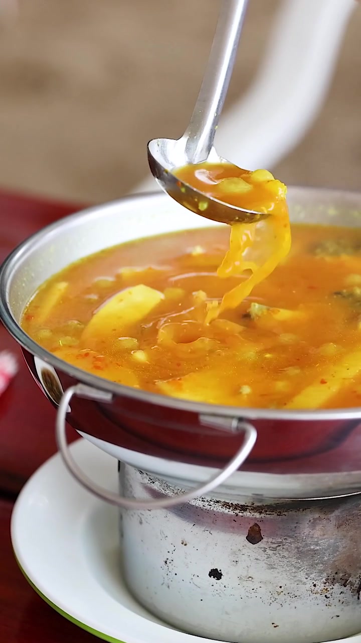 Un mestolo di metallo raccoglie e versa curry giallo aromatico all'interno di una tradizionale pentola calda riscaldata.