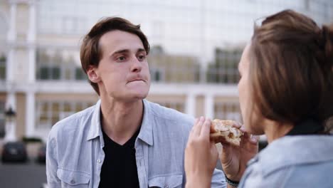 lovely young couple are eating a hamburger together.loving young people outdoors. wearing blue shirts. evening. park side