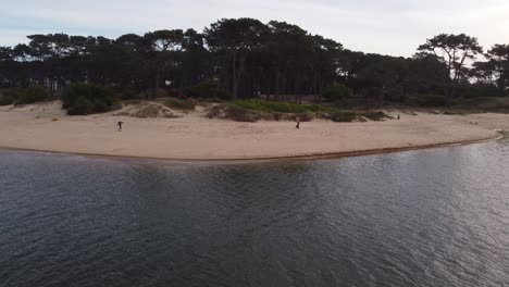 Drone-shot-of-young-boy-flying-kite-at-sandy-shoreline-at-Maldonado-River,Uruguay