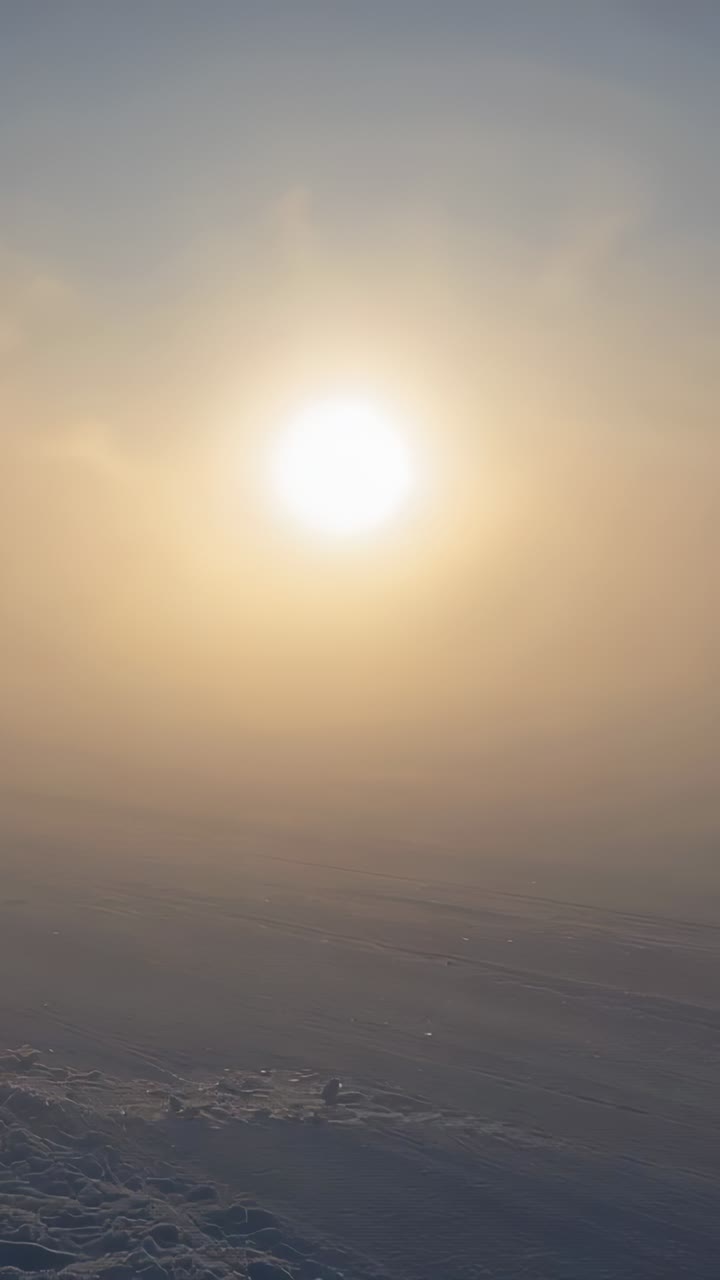 Vertical video: Shining sun creating halo over snow plain as camera tilting showing faint tracks
