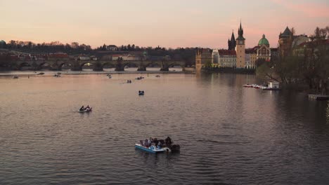 Pedal-boats-on-Vltava-river-with-beautiful-Charles-bridge-in-background,-romantic-evening