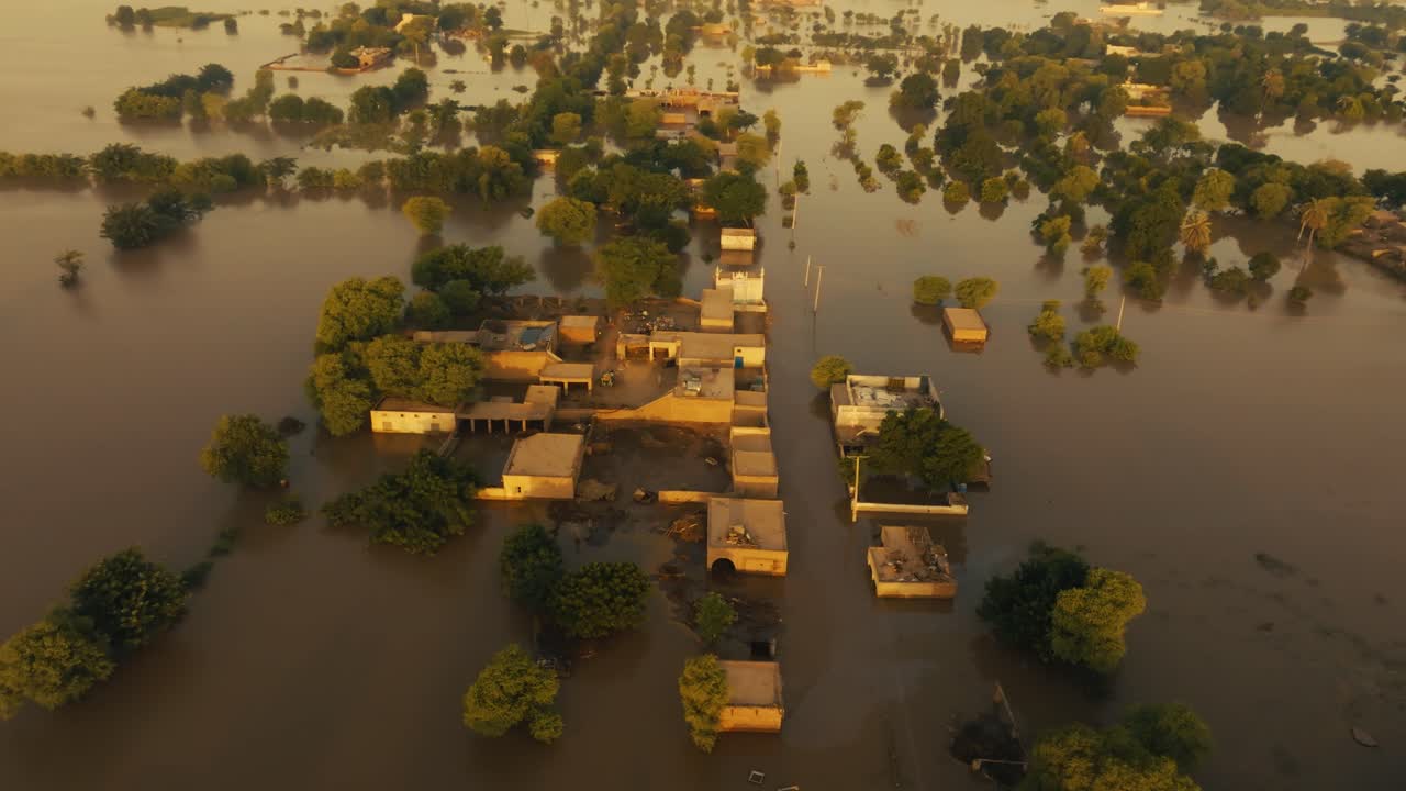 Aerial video over flooded fields and submerged houses in Jalalpur Pirwala, Pakistan, under sepia-toned late afternoon sun