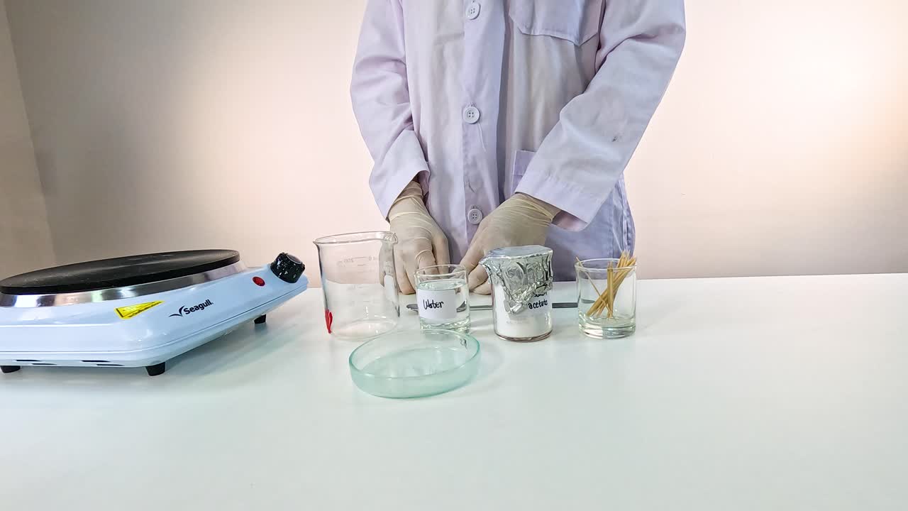 A scientist demonstrates sodium acetate crystallization using a hot plate and glassware in a well-lit laboratory setting