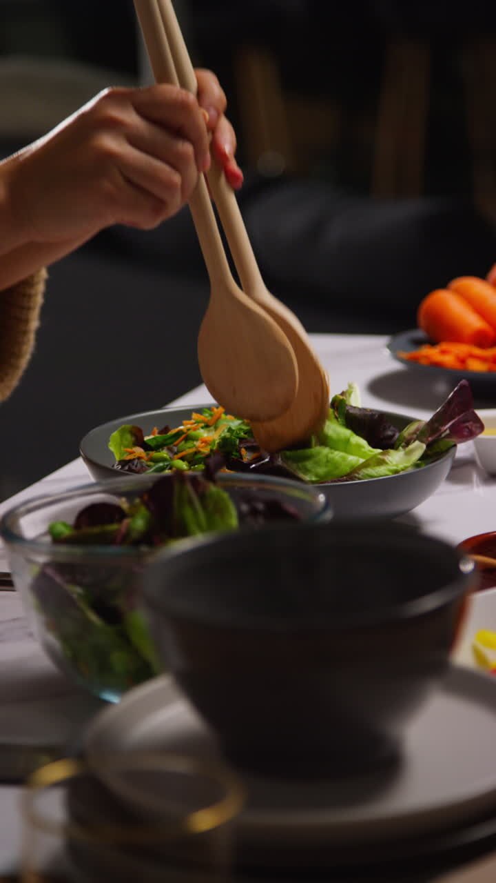 video vertical de cerca de una mujer en casa en la cocina preparando una comida saludable vegetariana o vegana mezclando hojas de ensalada en un cuenco