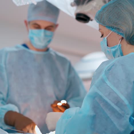 surgeons perform a surgery. specialist man and female assistant in blue medical uniform during operation in modern clinic.