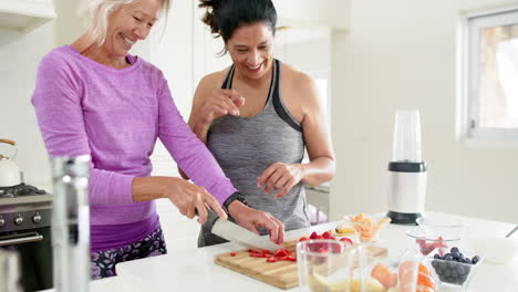 Zwei-Glückliche,-Vielfältige-Seniorinnen-Hacken-Obst-Und-Lachen-In-Einer-Sonnigen-Küche,-Zeitlupe