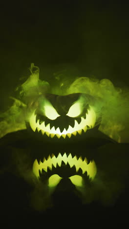 vertical video of halloween carved pumpkin with smoke and green light on black background