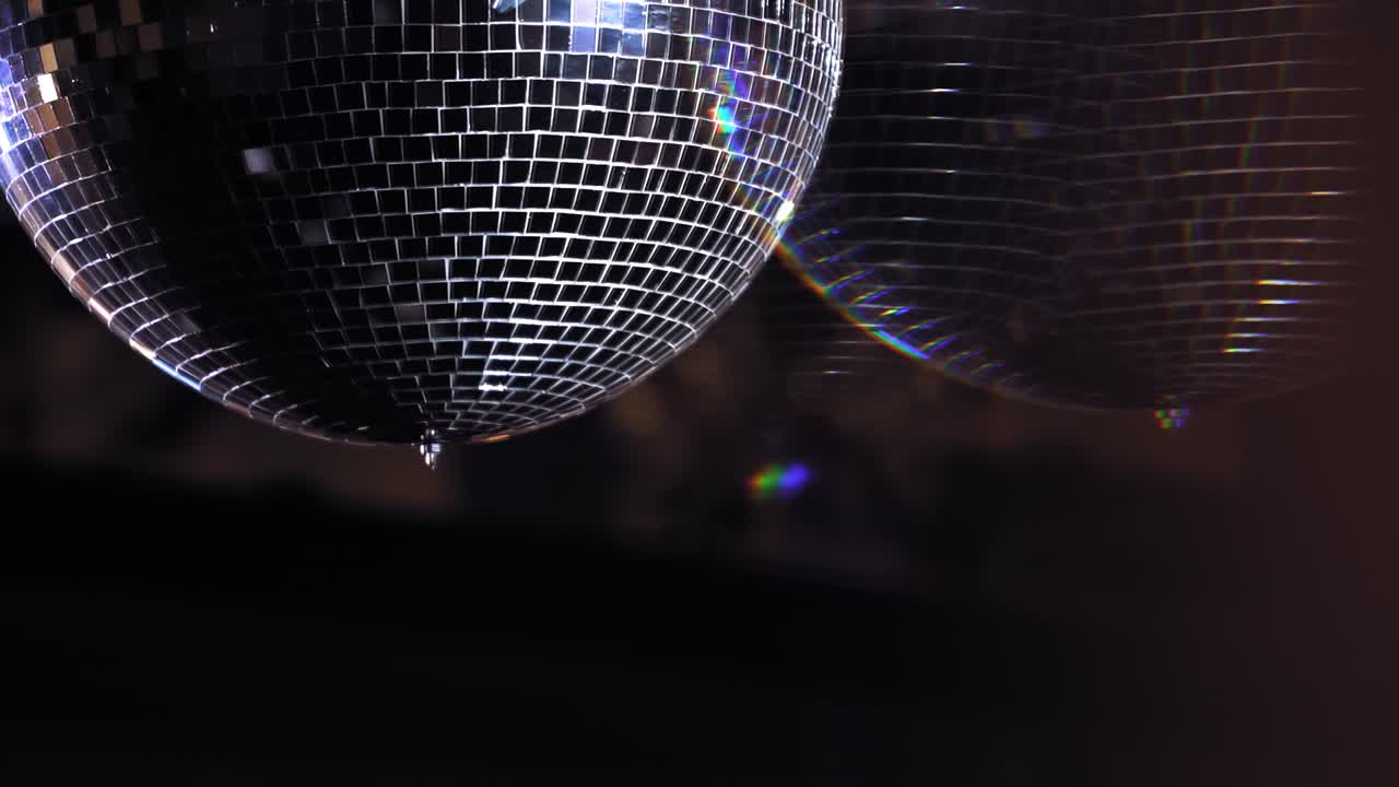 Mirror ball reflect rays of colored lights. Colorful reflective disco mirror ball with glinting highlights spinning slowly on a blurry background in disco club. The light show at night.