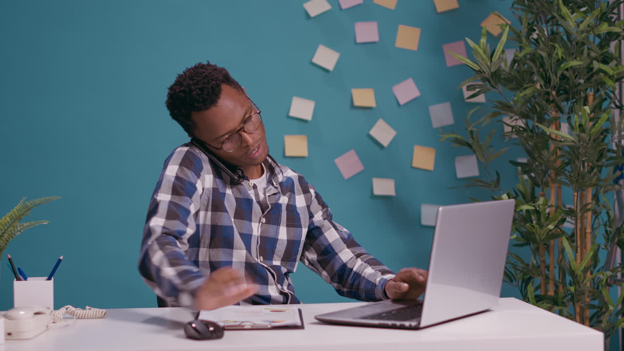 Office worker talking on phone call and using laptop to work
