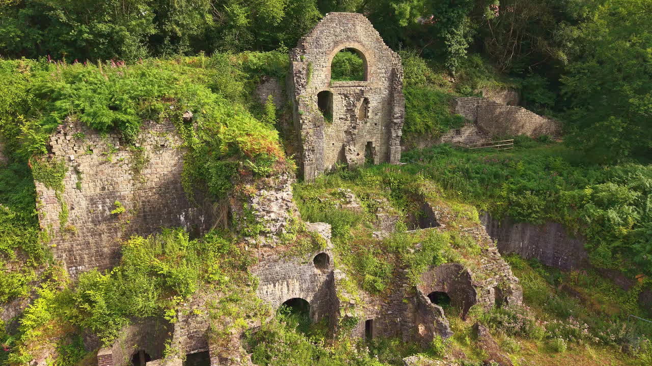 Slow aerial approach to the overgrown ruins of Clydach Ironworks in Wales