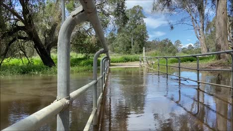 vista de ángulo bajo a través de las barandillas que miran a través de un puente peatonal inundado sobre un arroyo crecido después de la lluvia torrencial y la inundación en las inundaciones australianas en octubre de 2025
