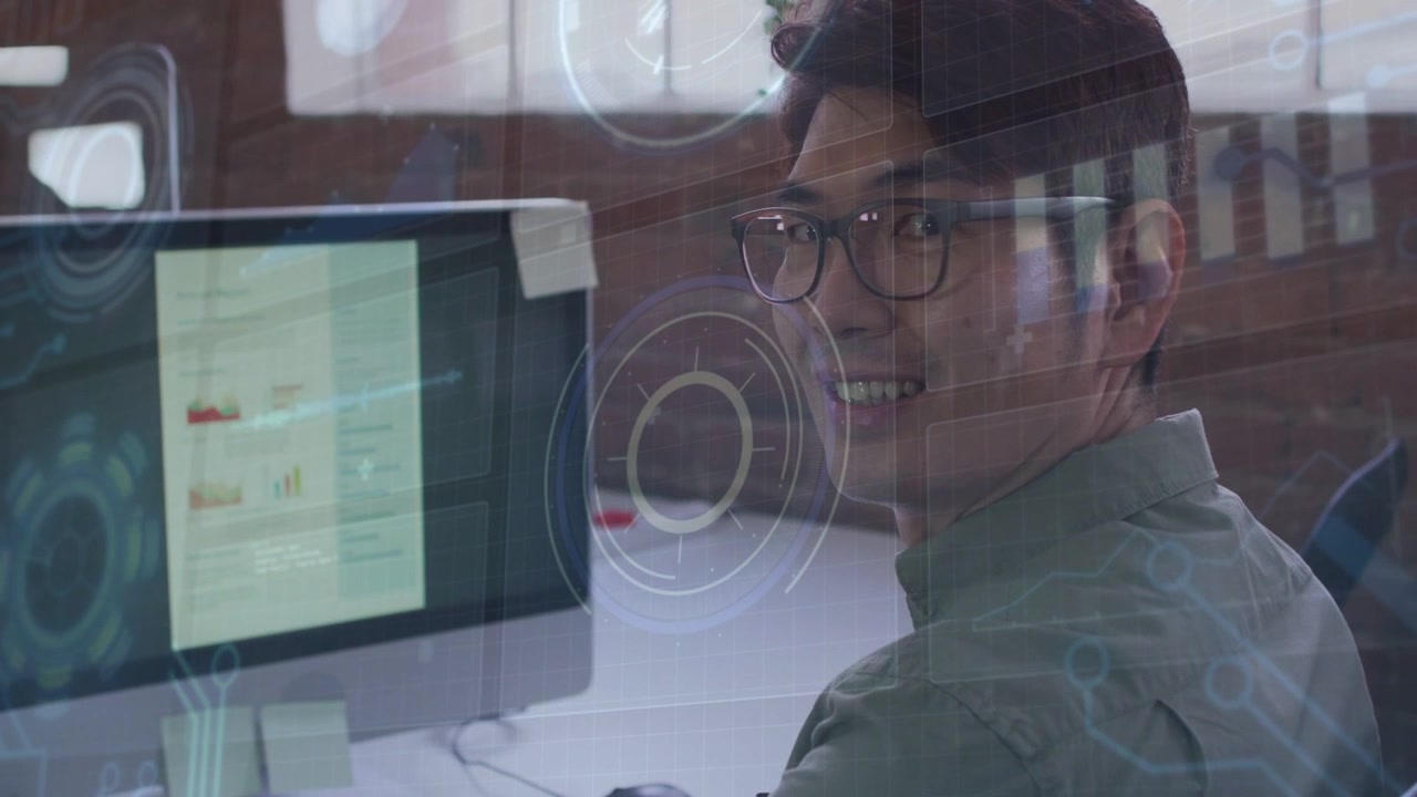 Male analyst typing at desk mousing HUD appearing on business charts stopping smiling at camera