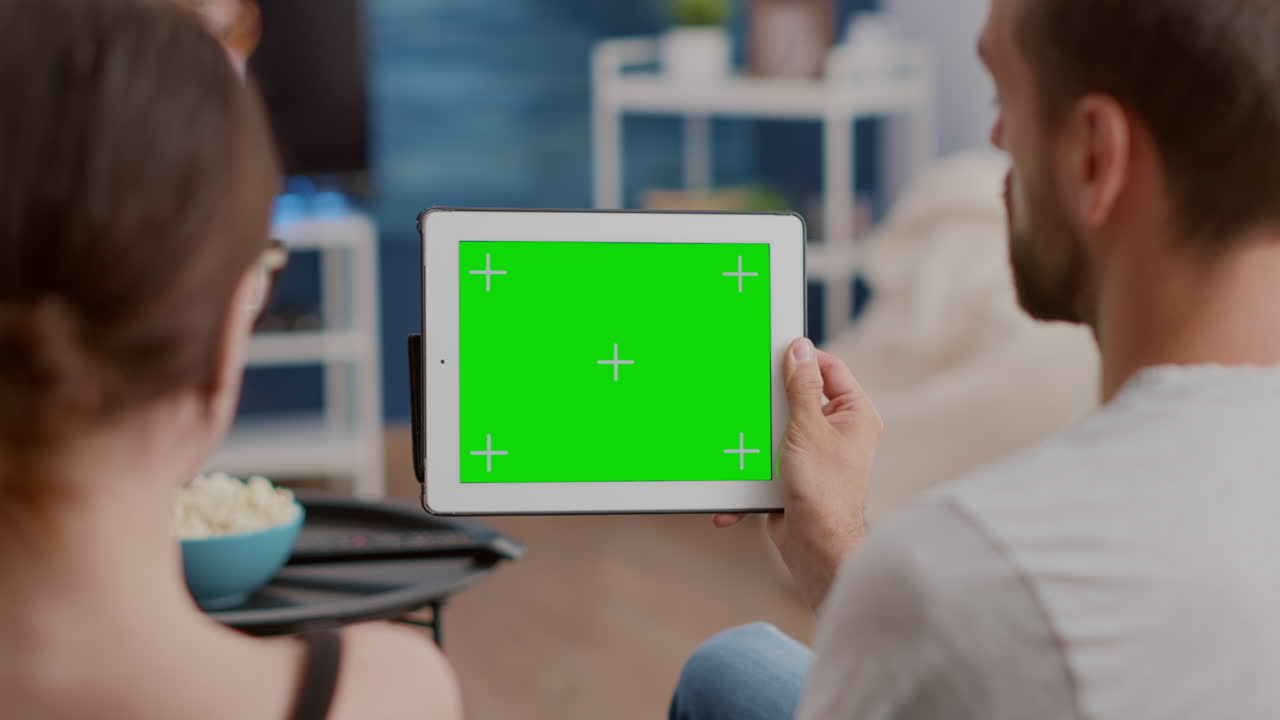Closeup of couple holding digital tablet with green screen watching webinar and talking