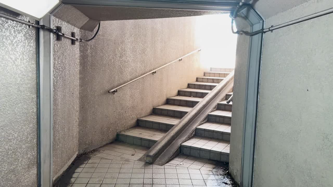A slow forward camera movement through a concrete pedestrian underpass toward bright outdoor light