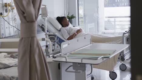 african american female patient lying in bed in hospital room, slow motion