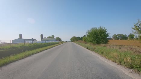 pov while driving past farmyards and field on a country road in rural iowa in late summer