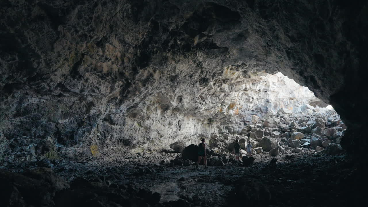 People exploring a large lava tube cave with natural light