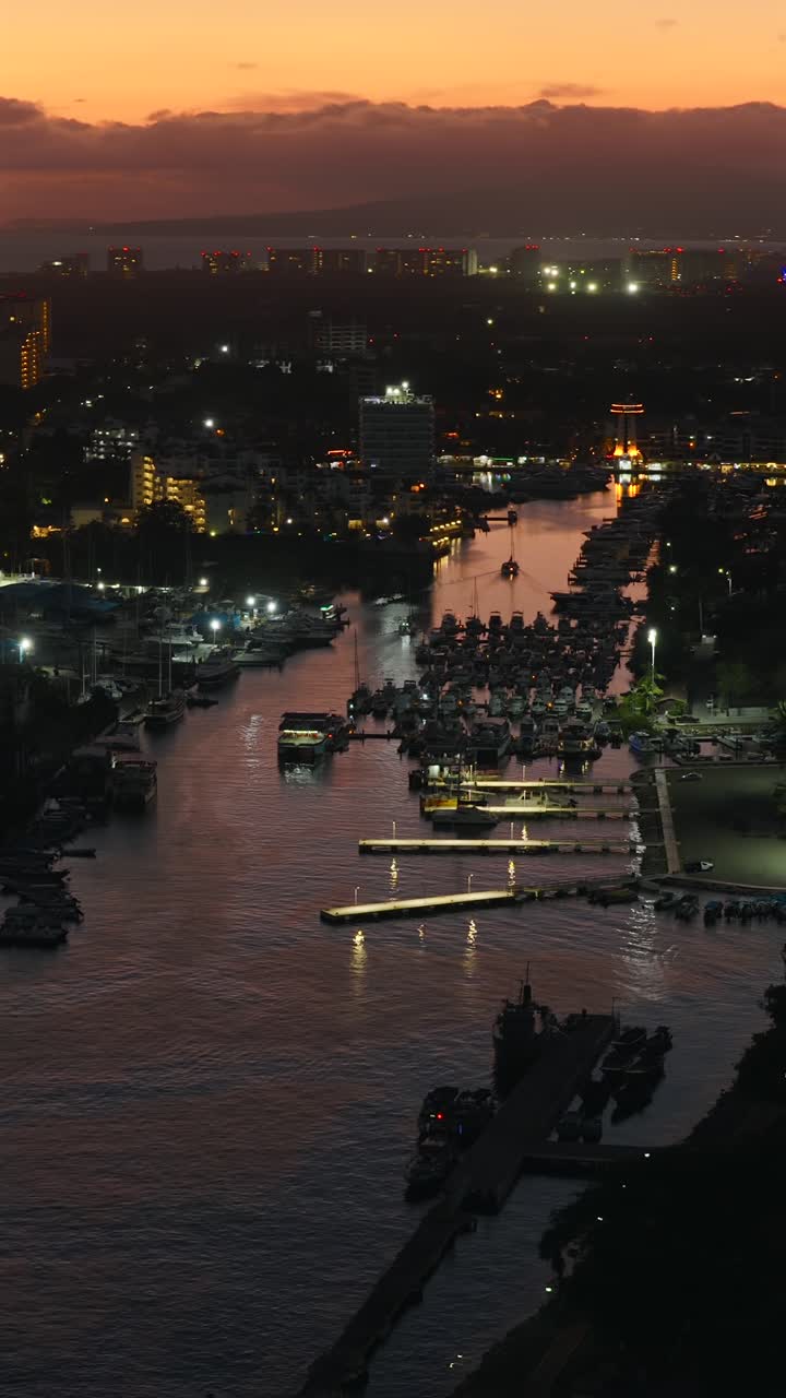 Stunning vertical aerial view of Marina Vallarta lined with yachts and docks, glowing under orange sunset sky. Puerto Vallarta, Mexico