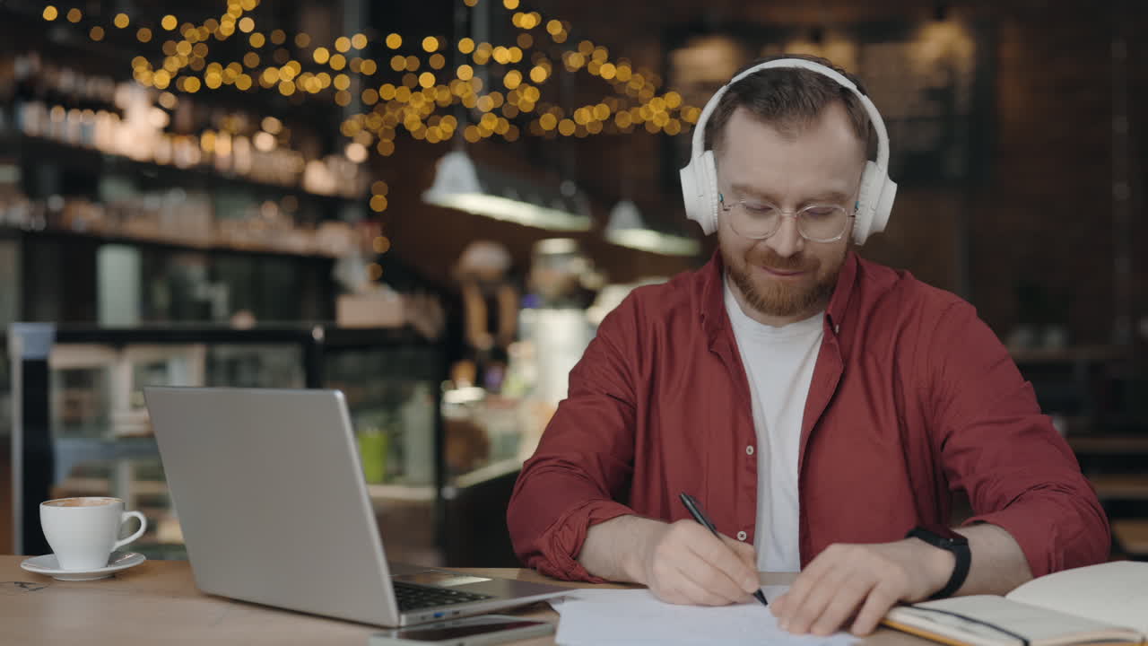Hombre trabajando en una cafetería con un portátil y auriculares