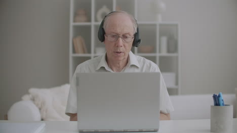 Ein-älterer-Männlicher-Professor-Kommuniziert-Per-Videoanruf-Von-Zu-Hause-Aus-über-Laptop-Und-Kopfhörer