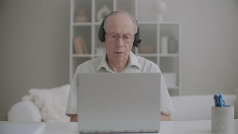 aged male professor is communicating by video call from home using laptop and headphones