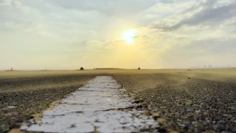 low view of fine sand particles blown by the wind on a highway in the middle of the desert at sunset