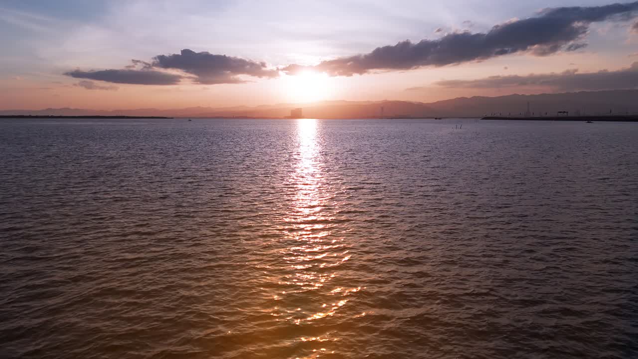 Cinematic view of the ocean at sunset with golden light reflecting on the water and distant mountains. Perfect for travel, lifestyle, cinematic, and inspirational projects