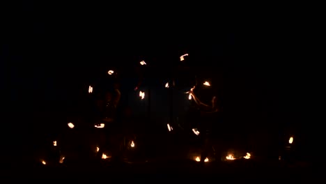 tres mujeres con aros ardientes bailan con antorchas ardientes en ropa de cuero en un hangar oscuro demostrando un espectáculo de fuego de circo en cámara lenta.