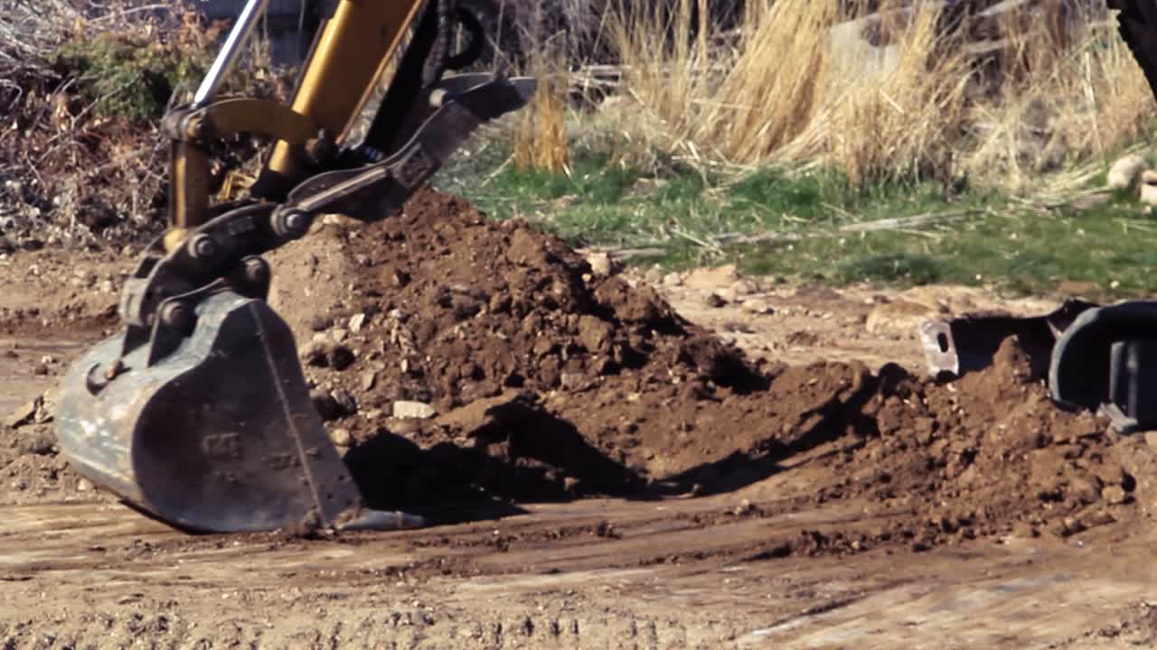 Excavator flattens the ground and adds to a pile of dirt.