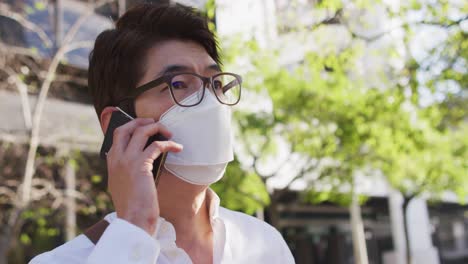 hombre asiático con máscara facial hablando en un teléfono inteligente en la calle