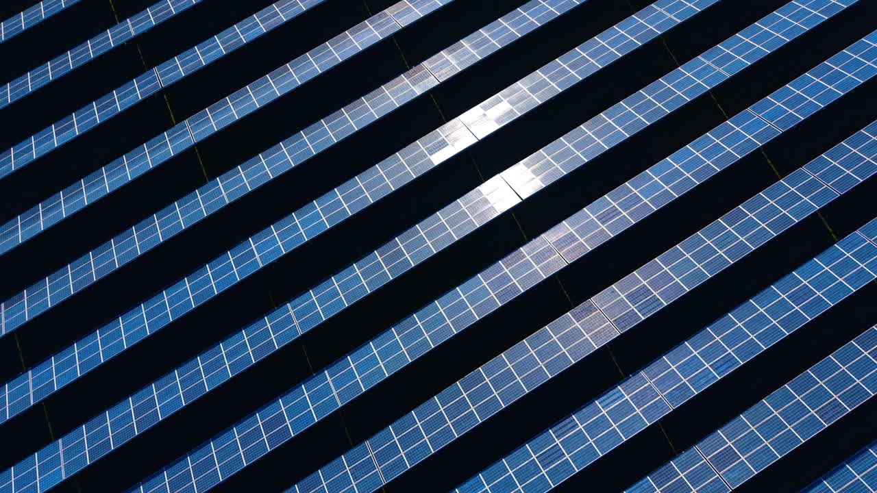 Vista dall'alto di un impianto solare con luce solare intensa. Moduli fotovoltaici in file con forte riflesso del sole su uno sfondo scuro, concetto di energia industriale aerea.