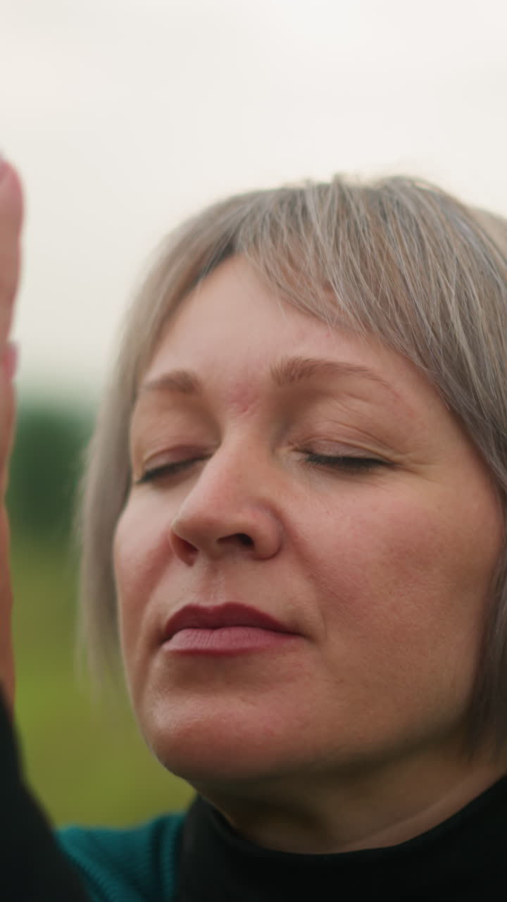 primer plano de una mujer en traje verde y negro en postura de cara de vaca, practicando yoga al aire libre en un campo de hierba brumosa, manos levantadas en un gesto meditativo con un fondo suave y borroso