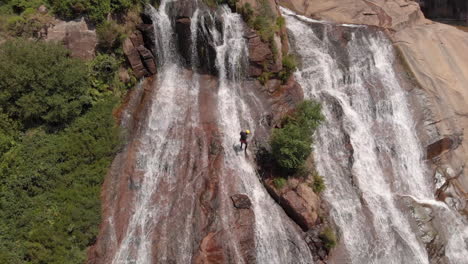 tourist rappelling down the rocky cliff at cascada de ezaro (fervenza do ezaro) in dumbria, spain. - aerial drone shot