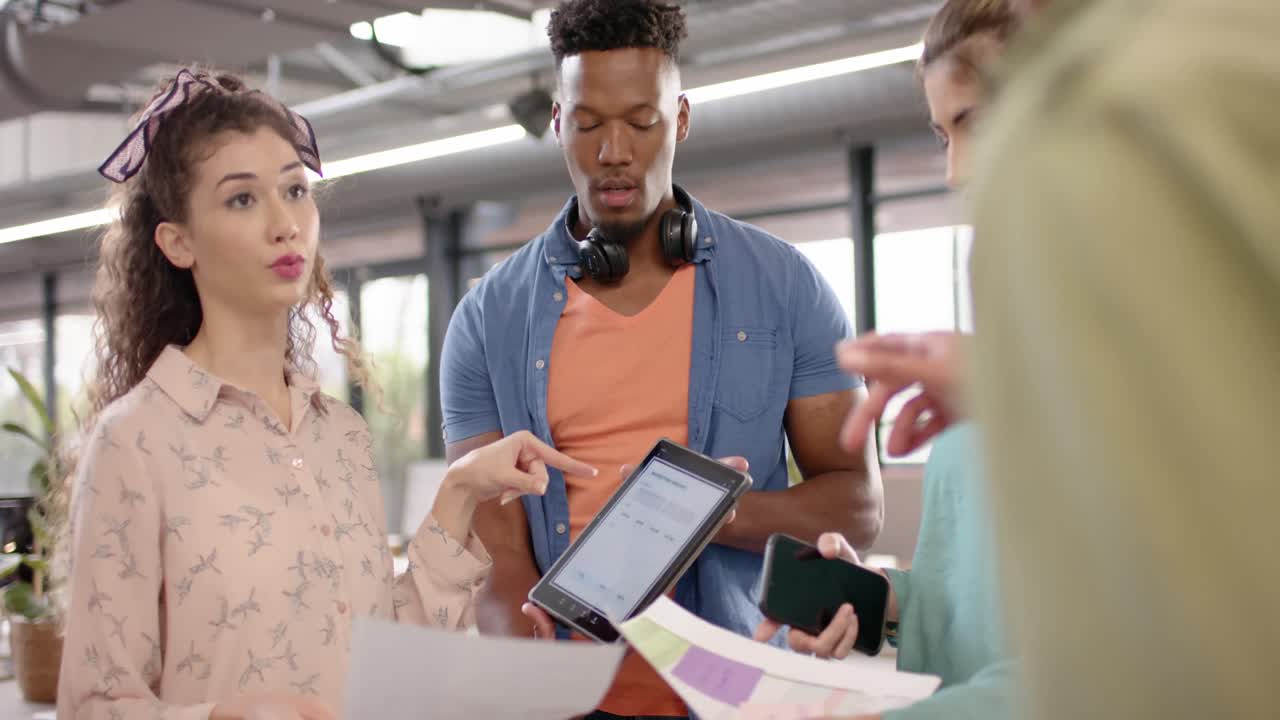 Happy diverse casual business colleagues with tablet and paperwork talking in office, slow motion
