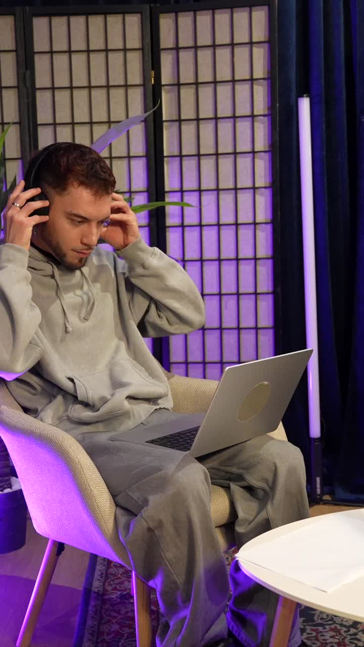 Young Man Puts on Headphones and Works on Laptop in Studio