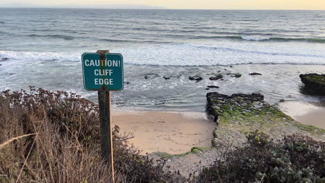 signo de precaución junto al mar en el borde del acantilado con olas rodando al anochecer, santa cruz con vistas a la bahía de monterey