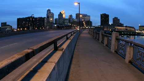 pedestrians and vehicles cross a bridge in downtown minneapolis as the evening sky darkens to night