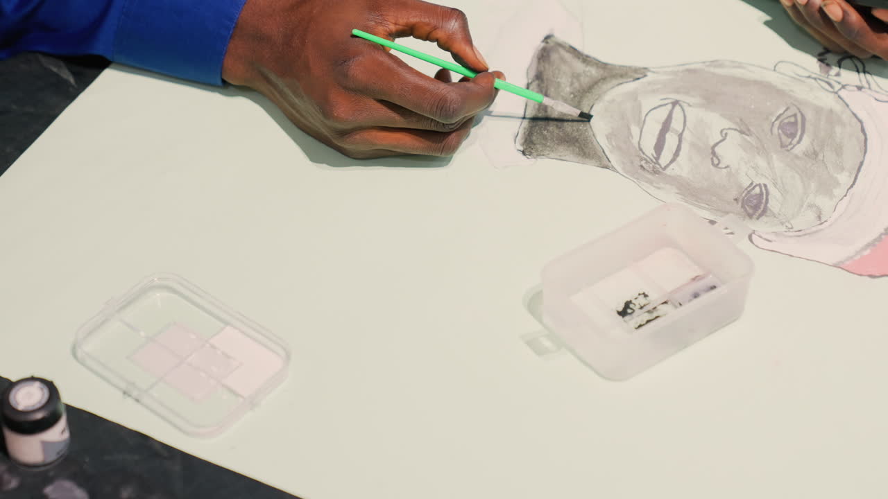 Black man portrait final touches overhead, commercial illustrator refining highlights with green pencil and palette, tabletop tools and ink bottle visible, polished modern studio vibe ready