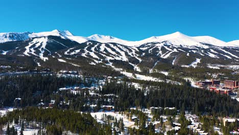 Vista-Aérea-Por-Drones-De-Picos-Montañosos-Cubiertos-De-Nieve-En-Invierno-Con-Pistas-De-Esquí-Listas-Para-Deportes-Al-Aire-Libre-Y-Aventuras-En-Un-Espeso-Bosque-De-Pinos