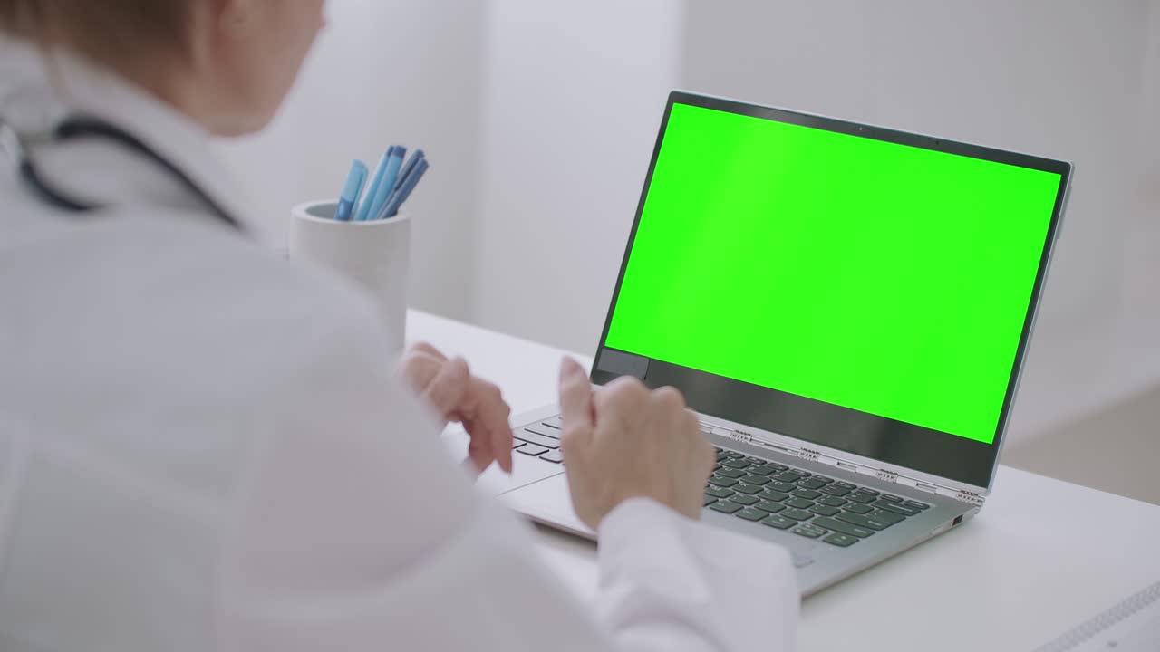 la mujer médico está mirando la pantalla verde de la computadora portátil para la tecnología chroma key, comunicándose en línea por chat de video o llamada de video