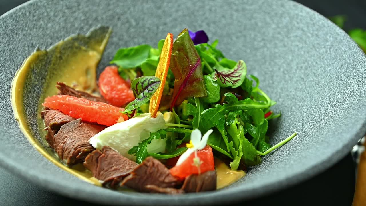 Fresh salad with fruit and dressing served in a dark bowl. A salad includes lettuce, grapefruit, and orange slices with dressing on a table