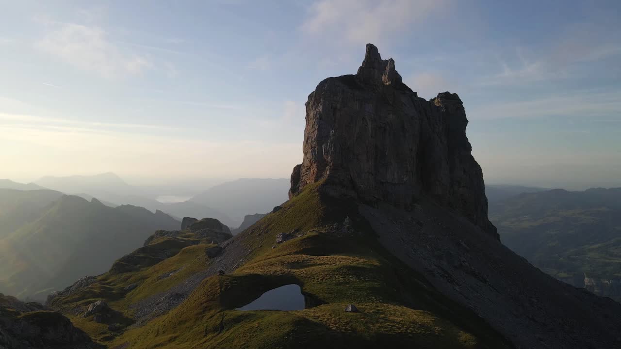 aerial footage Capturing the stunning Gross Achslenstock mountain peak in the swiss alps, bathed in warm sunset light, surrounded by expansive rolling hills and a serene sky, in Schwyz, Switzerland